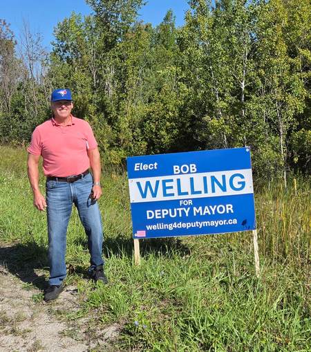 Bob Welling standing beside his Elect Bob Welling for Deputy Mayor campaign yard sign